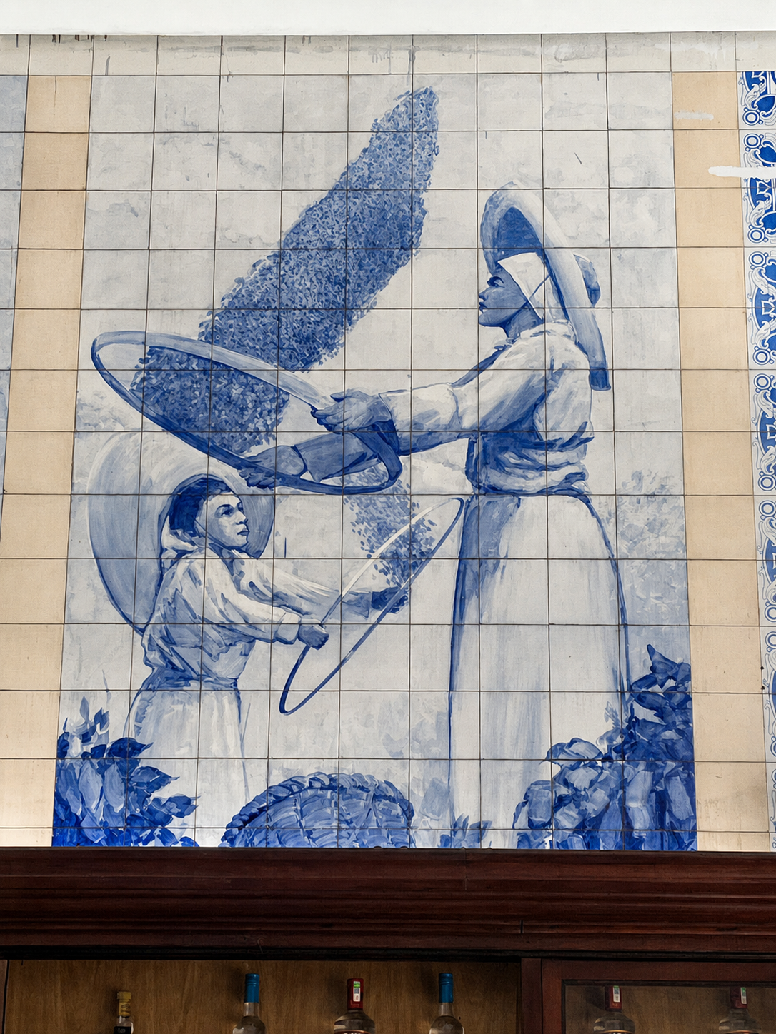 Painel pintado à mão em azulejos azuis retratando a colheita do café no Café Paulista de Santos